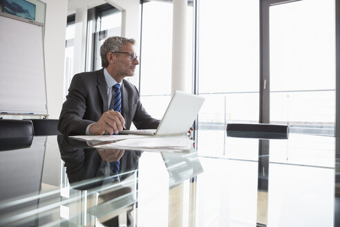 Älterer Manager sitzt im Büro und benutzt einen Laptop - RBF004356