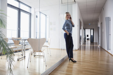 Businesswoman standing in office talking on the phone - RBF004373