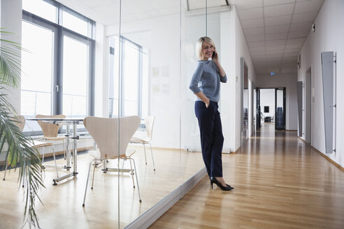 Geschäftsfrau steht im Büro und telefoniert - RBF004373