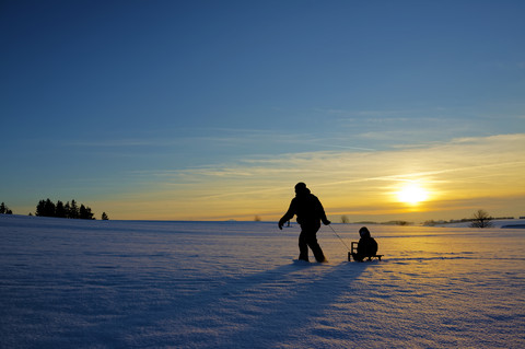 Mutter und Tochter beim Schlittenfahren bei Sonnenuntergang, lizenzfreies Stockfoto