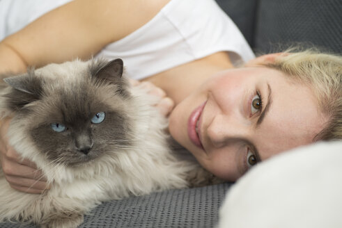 Porträt einer lächelnden jungen Frau, die mit ihrer Katze auf der Couch liegt - LFOF000205