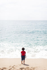 Rückenansicht eines kleinen Jungen, der am Strand steht und auf das Meer schaut - VABF000432