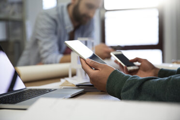 Man with portable devices at deskwith colleague in background - FKF001783