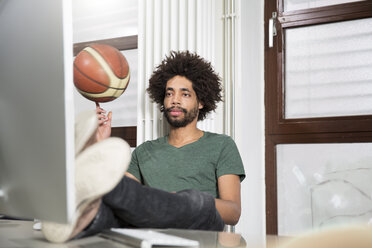 Creative professional balancing basketball at desk in office - FKF001832