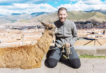 Peru, Cusco, Porträt eines glücklichen Touristen, der neben einem Lama kniet - GEMF000844