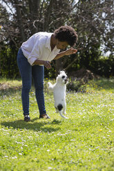 Young woman playing with her dog on a meadow - MAUF000431