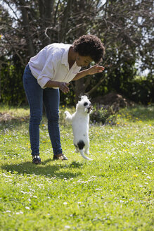 Junge Frau spielt mit ihrem Hund auf einer Wiese - MAUF000431