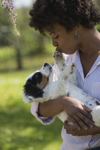 Junge Frau hält Hund in ihren Armen und küsst Pfote, lizenzfreies Stockfoto