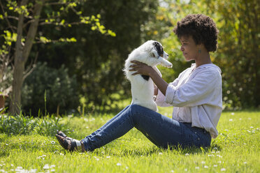 Junge Frau sitzt auf einer Wiese und spielt mit ihrem Hund - MAUF000437