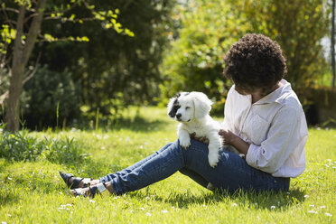 Young woman sitting on a meadow with her dog on lap - MAUF000439