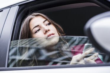 Brünette Frau sitzt im Auto und schaut durch das Fenster - UUF006856