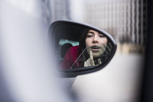 Pretty woman sitting in car applying make up in wing mirror - UUF006859