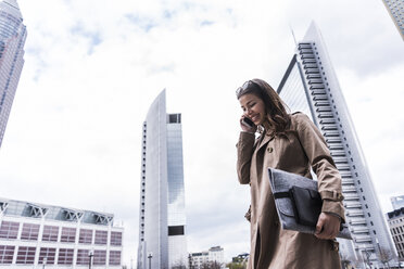Young businesswoman walking in city using mobile phone - UUF006880