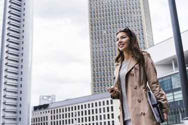 Young businesswoman walking in city using mobile phone - UUF006881