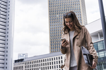 Young businesswoman walking in city using mobile phone - UUF006882