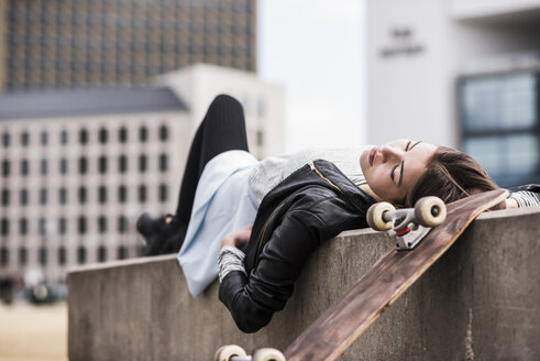 Junge Frau mit Skateboard an der Wand lehnend - UUF006902