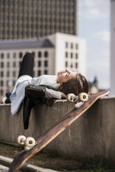 Junge Frau mit Skateboard an der Wand lehnend - UUF006903