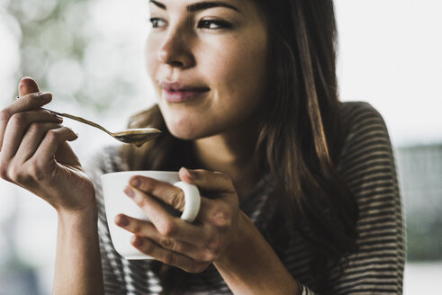 Junge Frau trinkt Cappuccino, löffelt Milchschaum - UUF006907