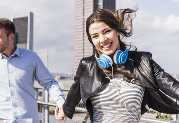 Glückliches junges Paar, Frau springt mit Kopfhörern um den Hals - UUF006924