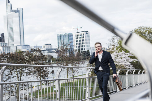 Young businessman walking in the city, talking on the phone - UUF006935