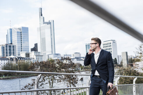 Junger Geschäftsmann, der in der Stadt spazieren geht und dabei telefoniert - UUF006936