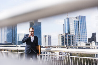 Junger Geschäftsmann, der in der Stadt spazieren geht und dabei telefoniert - UUF006938