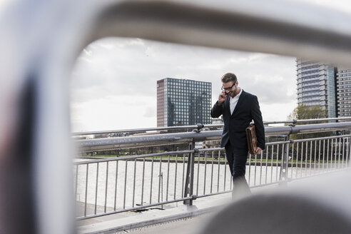 Junger Geschäftsmann, der in der Stadt spazieren geht und dabei telefoniert - UUF006939