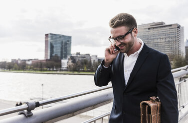 Young businessman walking in the city, talking on the phone - UUF006941