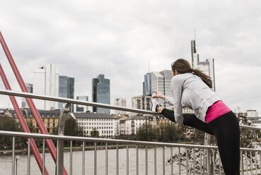 Young woman jogging in the city, stretching leg - UUF006961