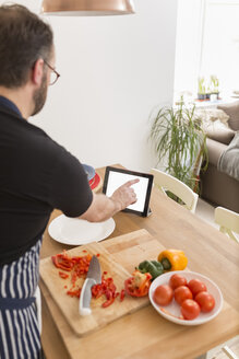 Mann mit digitalem Tablet bei der Zubereitung von Speisen in der Küche - BOYF000252