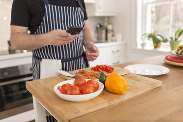 Mann benutzt Smartphone bei der Zubereitung von Speisen in der Küche, Teilansicht - BOYF000255