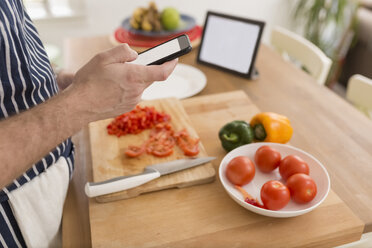 Mann benutzt Smartphone bei der Zubereitung von Speisen in der Küche, Nahaufnahme - BOYF000256