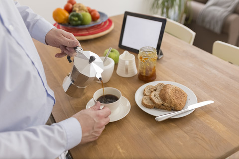 Mann gießt Espresso in eine Tasse am Frühstückstisch, Teilansicht, lizenzfreies Stockfoto