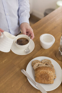 Mann gießt Milch in eine Kaffeetasse am Frühstückstisch, Teilansicht - BOYF000275