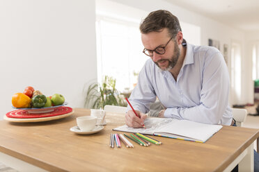 Man with colouring book and coloured pencils sitting at wooden table - BOYF000283