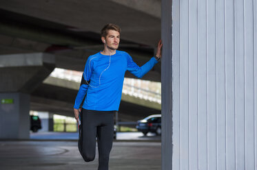 Junger sportlicher Mann beim Stretching, Smartwatch und Kopfhörer - DIGF000239