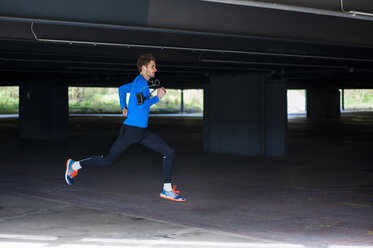 Junger sportlicher Mann beim Joggen mit Smartwatch und Kopfhörern - DIGF000243