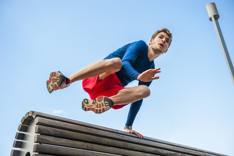 Junger sportlicher Mann springt über eine Bank, lizenzfreies Stockfoto