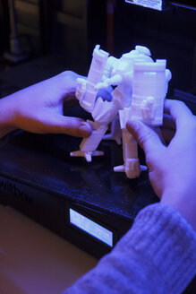 Hände nehmen eine 3D-Roboterfigur aus einem 3D-Drucker - ABZF000343
