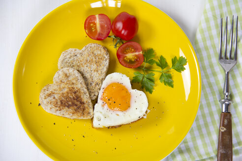 Fried egg in heart shape, toasts, cherry tomatoes on yellow plate - YFF000538