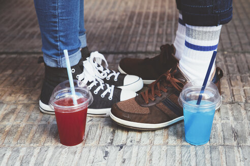 Plastic cups with soft drinks standing besides feet of young couple - RTBF000113