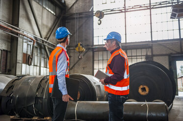 Two men with safety vests in factory hall with rolls of rubber - DIGF000272