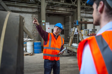 Mann mit Sicherheitsweste in einer Fabrikhalle, der mit dem Finger zeigt - DIGF000276