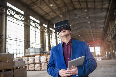 Manager steht in einer Fabrikhalle und schaut durch eine VR-Brille - DIGF000302