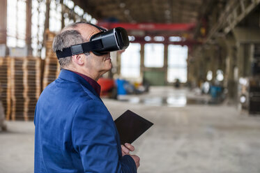 Manager standing in factory hall looking through VR glasses - DIGF000303