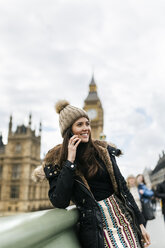 Großbritannien, London, glückliche junge Frau telefoniert mit Smartphone vor dem Palace of Westminster - MGOF001727