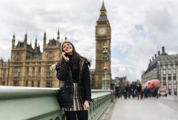 Großbritannien, London, glückliche junge Frau telefoniert mit Smartphone vor dem Palace of Westminster - MGOF001728