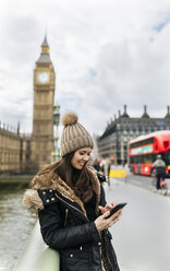 Großbritannien, London, lächelnde junge Frau schaut auf ihr Smartphone vor dem Palace of Westminster - MGOF001729