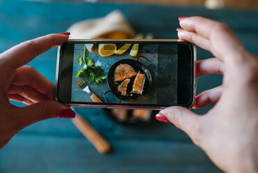 Closeup of hands taking a picture of salmon fillets with parsley and lemon - KIJF000325