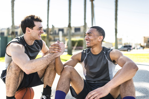 Zwei junge Männer schütteln sich auf einem Basketballplatz im Freien die Hände, lizenzfreies Stockfoto